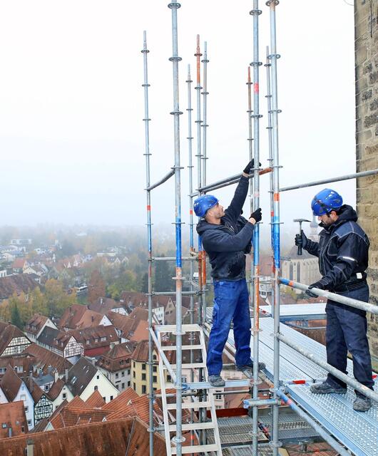 Im Laufe von 2017 fällt der Startschuss für das Mammut-Projekt. In einem ersten Schritt wird der Blaue Turm eingerüstet. Deshalb grüßt Türmerin Blanca Knodel ab Oktober täglich die Gerüstbauer, wenn die in ihrem Aufzug aus Metall an ihrem Turmfenster vorbeifahren. Durch die Verbindung von Eisenstangen und -riegeln arbeiten sich Manuel Bergmann, Massimo Dimauro und Mehmet Taskiran bis zur Turmhaube in rund 30 Metern Höhe hoch.