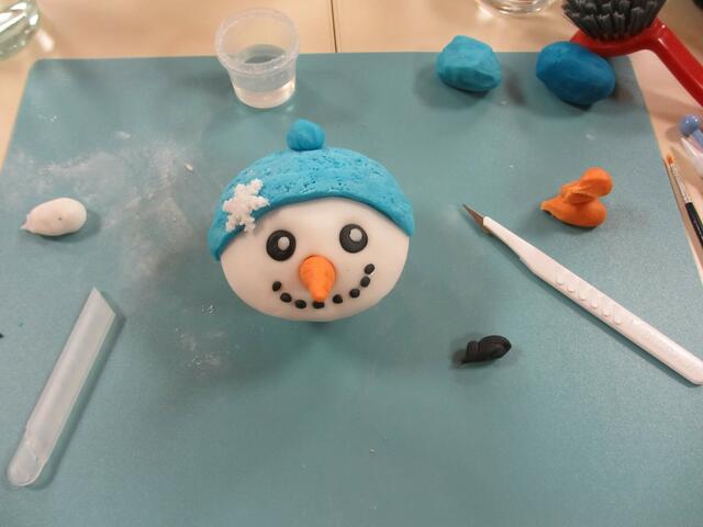 Fondant in bunten Farben, geeignetes Werkzeug und viel Fingerspitzengefühl - fertig ist ein Cupcake mit Schneemanngesicht.