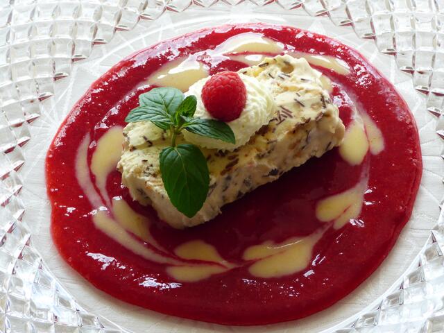 Das Parfait auf dem Himbeerspiegel anrichten und nach Lust und Laune mit Sahnetupfen, Himbeere und Minzblatt dekorieren.