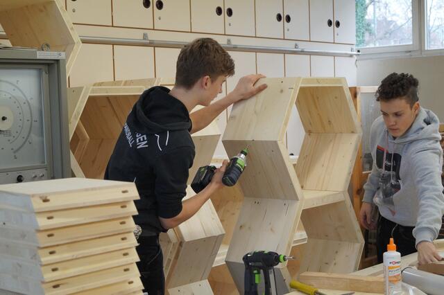 Auszubildende im Zimmererhandwerk fertigen Holzelemente für die Wabenwand in den Werkstätten der beruflichen Schule an.