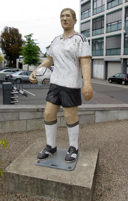 https://www.kunst-whgsinsheim.de/kunst-und-theater/kunst-in-sinsheim/Zitat Wilhelmi-Gymnasium Sinsheim: "Dank Christel Lechner haben wir in Sinsheim ein weiteres Erinnerungsobjekt an die Frauen-Fußball-Weltmeisterschaft. Auch im Rahmen des WM-Kulturprogramms wurden fünf lebensgroße Alltagsmenschen auf dem Platz vor der Volksbank platziert. Sie betrachten die Anzeigentafel der Bank, ruhen sich auf den Mauer sitzend aus oder Betrachten das im Folgenden vorgestellte neueste Kunstwerk Sinsheims - die Hausgeburt