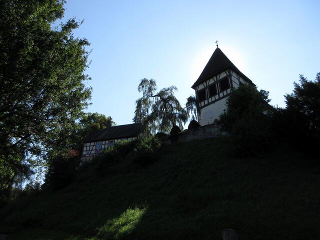 Walterichskirche, am Nachmittag steht die Sonne hinter der Kirche. Zum Walterichshügel führt eine Pilgerstaffel hinauf. Bei einer weiteren Gelegenheit lohnt sich auch ein Historischer Stadtrundgang in Murrhardt