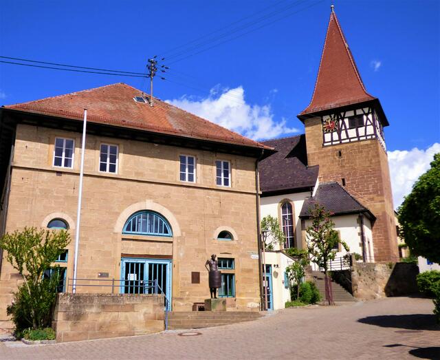 Die kleine Ortsmitte von Haberschlacht mit Rathaus und Kirche. Vor dem Rathaus steht der "Mann im Fass".
