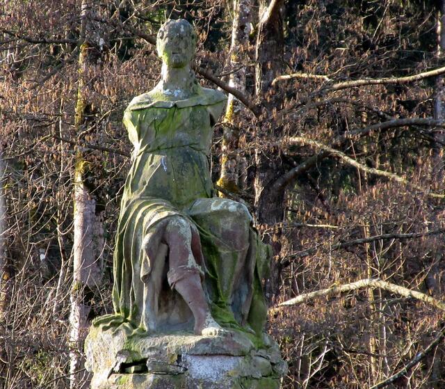 Text vom Schild: Sandsteinstatue der Göttin Diana oder Kybele. Davon leitet sich "Das Kibannele" im Volksmund ab. Die Statue ist einziger Zeuge eines Tiergartens mit Seeanlage und Lustschloss, den Herzog Eberhard III hier auf 200 Morgen anlegen ließ.
