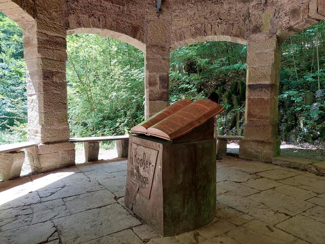 Hier erwartet die Wanderer ein schattiges Plätzchen, der Brunnen zum Füße kühlen und eine spannende Geschichte.