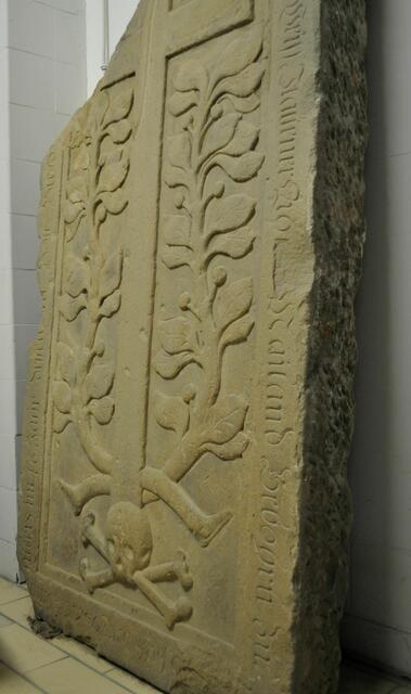 Grabplatte des Andoni Weiss (Bianchi) (+ Dez. 1708). Dargestellt ist ein Kreuz, eingerahmt von Lorbeerzweigen?, über einem Totenschädel und zwei gekreuzten Knochen. 
Es handelt sich um ein altes biblisches Motiv: Der Schädel Adams und seine Gebeine, die durch das Erdbeben, das beim Tode Christi einsetzte, am Fuße des Kreuzes zutage getreten seien. Der Stammvater Adam wird in dem Zusammenhang als "alter Adam" und der das ewige Leben bringende Erlöser Jesus Christus als "neuer Adam" bezeichnet. Diese allegorische Bildlösung stellt den Bezug zwischen Altem und Neuem Testament dar. Der Schädel Adams findet sich deshalb in der christlichen Kunst häufig am Fuße von Kruzifixen. 
Quelle: Heilbronner Stadtarchiv | Foto: Daniela Somers