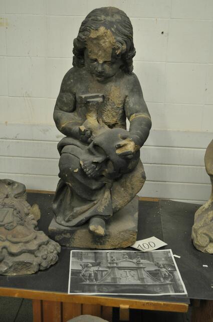 Sitzender Putto mit Totenschädel und Sanduhr vom Siebenröhrenbrunnen. 
Die Figur befand sich als mittlere (von dreien) ganz oben auf dem Tympanon des neuen Siebenröhrenbrunnes von 1904.
Beim Wiederaufbau des Brunnens nach dem Krieg, wurden diese Putten wie auch die beiden Ritterfiguren die seitlich waren, weggelassen.

 | Foto: Daniela Somers