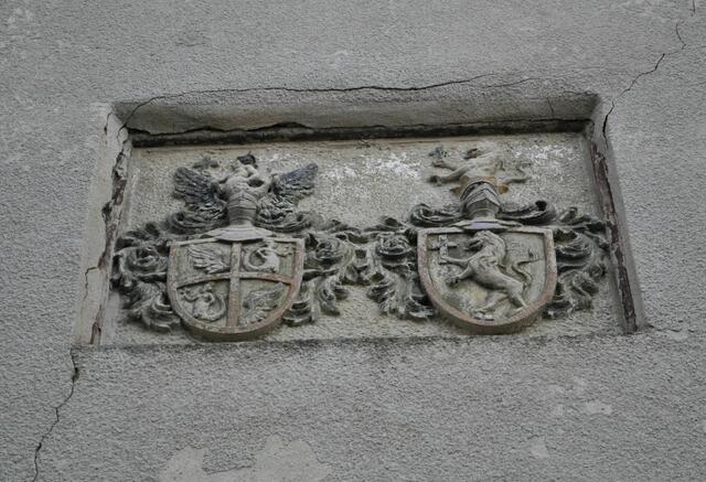 Das Allianzwappen der Eheleute Bonifatius Rieker und Anna Elisabeth Rieker an einer Hauswand. Dem Gatten ist das Wappen mit dem Fischweib und der Ehefrau der aufsteigende Löwe zuzuordnen. Das Wappen mit seinem viergeteilten Feld und der Frauenfigur soll an das Wappen des damaligen Mömpelgard/Montbeliard bei Belfort (bis zur Französischen Revolution württembergischer Besitz) erinnern. Von der ehemals fränkischen Hofanlage ist aber sonst nichts fotogenes mehr übrig geblieben. | Foto: Daniela Somers