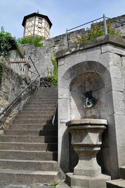 Ein altes Taufbecken als Brunnentrog am Aufstieg zur Kirche. Rechts würde es weiter gehen zum Eingang in der Burgmauer. | Foto: Daniela Somers