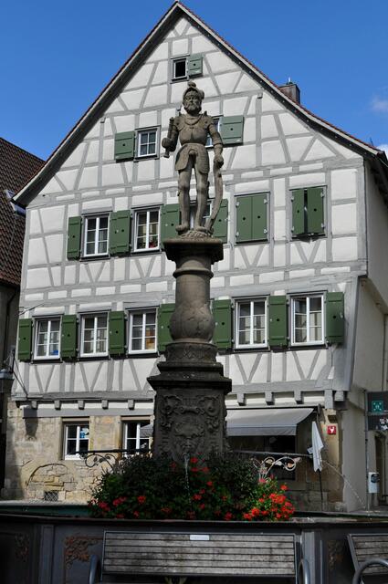 Der Marktbrunnen. 1866 wurde der steinerne Trog durch einen gusseisernen Trog ersetzt. Eine vier Kilometer lange Wasserleitung speiste den Brunnen. Hier wurde Wasser geholt. Das Vieh getränkt. Aber auch an Markttagen die Fische frisch gehalten. Sie wurden einfach in Netzen in den Brunnen gehängt.
dahinter ein Wohn-und Geschäftshaus, dass im Kern auf das Jahr 1519 zurück geht. | Foto: Daniela Somers