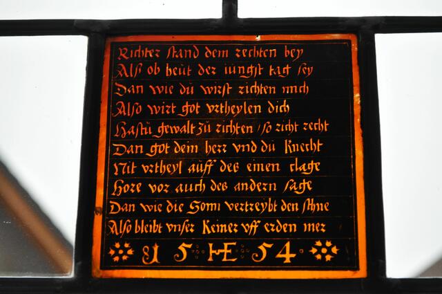 Im Rathaus innen gibt es nicht viel zu sehen. Knarzende alte Dielen sind noch vorhanden. Ansonsten sieht alles recht neu aus. Dieser Spruch in Glas verewigt kann man sich noch anschauen. Er ist von 1554 und wohl vom damaligen Schulmeister und Notar Hieronymus Esslinger gestiftet. Wer es lesen möchte: Richter stand dem rechten bey / Alß ob heut der iungst tag sey / dan wie du wirst richten mich / Also wirt got vrtheylen dich / Hastu gewalt zu richten, so richt recht / Dan got dein herr vnd du Knecht / Nit vrtheyl auff des einen clage / Hore vor auch des andern sage / Dan wie die sonn vertreybt den Schne / Also bleibt vnser keiner vff erden mer / 15 HE 54.  | Foto: Daniela Somers