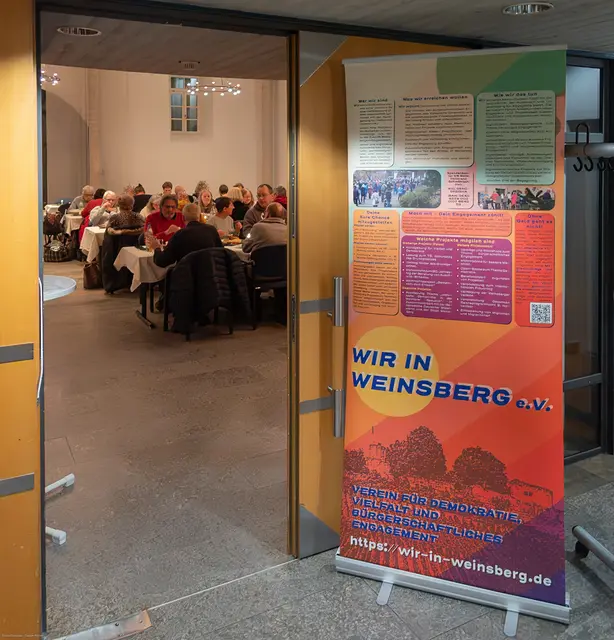 Blick in den Veranstaltungsraum während „Gemeinsam statt einsam“.
Das Roll-up von „Wir in Weinsberg e. V.“ weist auf das bürgerschaftliche Engagement des Vereins hin. | Foto: Wir in Weinsberg e.V