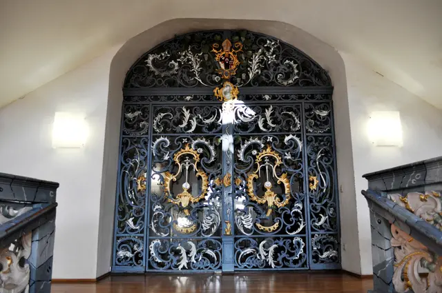 Prächtiges Gitter aus Schmiedeeisen. Abt Augustin Brunnquell (regierte 1761 bis 1784) gab es in Auftrag. Sein Wappen,  ein aus einem Füllhorn quellender Springbrunnen, sieht man auf beiden Torflügeln. | Foto: Daniela Somers