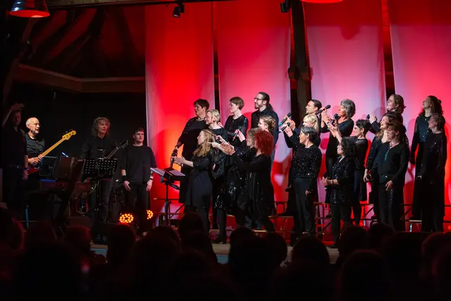 Chor steht auf der Bühne, wendet sich der Band zu und klatscht ihr Beifall