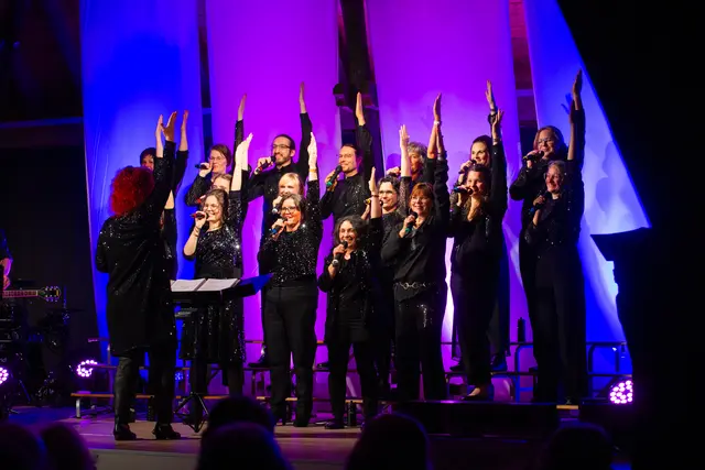 Chor auf der Bühne singt und hält die Hand gestreckt nach oben als Teil der CHoreographie