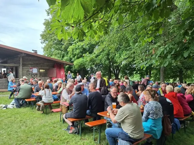 Viele Menschen sitzen auf Bierbänken am Waldrand zusammen