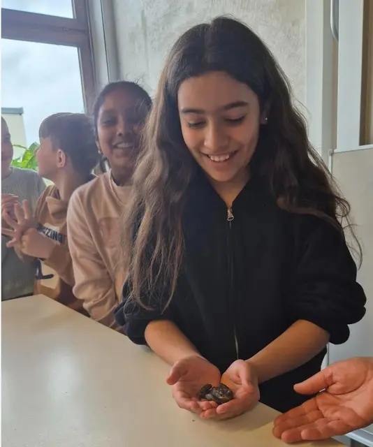 Eine Schülerin hält die Kröte auf beiden Händen. Dahinter stehen schon Schüler Schlange, die die Kröte auch auf der Halt halten möchten.