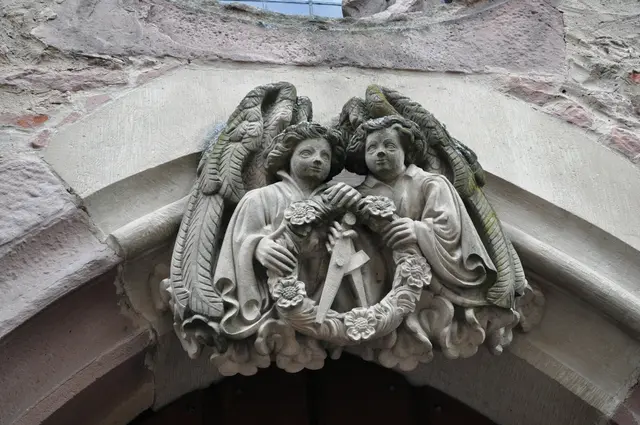 Diese zwei Jünglinge in Gestalt von Engeln tragen einen Zirkel. Der Legende nach verunglückten die Zwillingssöhne des Baumeisters beim Sturz vom Baugerüst. Er verewigte sie auf diesem Relief und sich selbst mit dem Symbol des Zirkels. Dieses Relief ist am Ruprechtsbau zu sehen. | Foto: Daniela Somers
