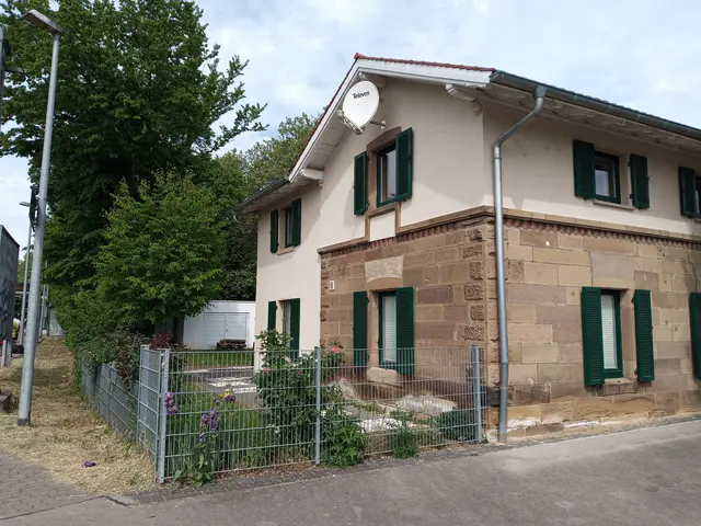 Das Bild zeigt das Beratungshäusle der Heilbronner Bezirksgruppe des BSV-Württemberg e.V. aufgenommen aus Richtung der S-Bahnhaltestelle "Sonnenbrunnen". Es handelt sich um ein ehemaliges Bahnwärterhaus, so wie sie zu Beginn des 19. Jahrhunderts gebaut wurden. Vor den Haus sieht man den Garten mit Sträuchern und einigen Blumen.