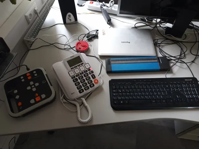 PC-Arbeitsplatz für eine blinde oder stark sehbehinderte Person mit Notebook, Tatatur, Braillezeile und Lautsprecher für die Sprachausgabe. Daneben das Targa-Seniorentelefon und ein Daisyplayer.