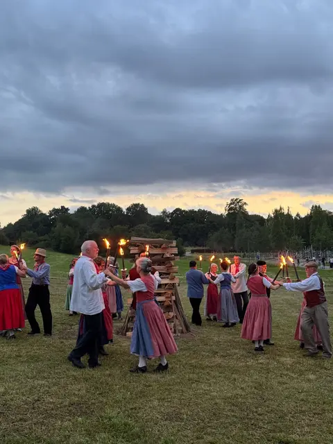 Menschen in traditionellen Kleidern beim Tanzen um einen Holzscheit.